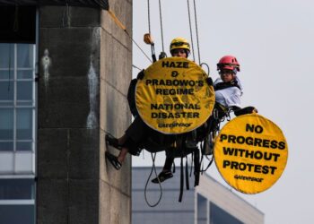 AKTIVIS Greenpeace Indonesia yang bergayut pada Patung Selamat Datang di Bulatan Hotel Indonesia memegang sepanduk membantah jerebu di Jakarta semalam. - AFP.