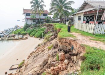 ROSHAILA Abdullah melihat hakisan tebing di belakang kedainya di Kampung Pantai Batu Rakit, Kuala Nerus, Terengganu. – UTUSAN/PUQTRA HAIRRY