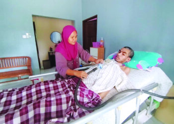 ROSLIZA Wahid menguruskan Tawaka Ab. Ghani yang terlantar selepas terkena jangkitan kuman pada selaput otak di Kampung Bukit Jeruk, Besut, Terengganu. – UTUSAN/WAN ZURATIKAH IFFAH WAN ZULKIFLI
