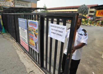 SEORANG pengawal keselamatan menutup pagar yang telah ditampal notis penutupan sekolah akibat jerebu di SMK Bandar Baru Uda, Johor Bahru, Johor hari ini.-UTUSAN/RAJA JAAFAR ALI