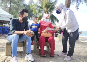 DR. Hadijah Baba (kanan) menyampaikan risalah berkaitan AADK kepada orang ramai yang beriadah bersama ahli keluarga di Pantai Telok Kemang, Port Dickson hari ini.-UTUSAN/BADRUL HAFIZAN MAT ISA