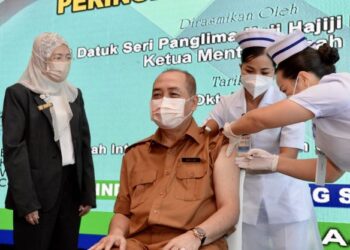 HAJIJI Noor menerima dos penggalak sambil diperhatikan oleh Pengarah Kesihatan Negeri Sabah, Datuk Dr. Rose Nani Mudin (kiri)