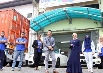 Nurul Hassrah Mohd Khori (tiga dari kanan) dan Mohd Hafiz Arbaee bergambar depan kilang bersama sebahagian pekerja syarikatnya.
