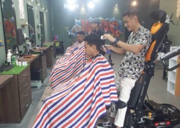 MOHAMAD Arif Ahmad menggunakan kerusi roda hidraulik ketika menggunting rambut pelanggan di kedainya di Taman Gembira, Bukit Batu, Kulai, Johor.