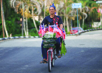 MOHD. Amin Ahmad mengayuh basikal yang dihiasi dengan Jalur Gemilang bagi menjual petai sebagai simbolik cintanya pada negara sempena ulang tahun kemerdekaan ketika ditemui di Stesen Kereta Api Wakaf Bharu, Tumpat, Kelantan. - UTUSAN/KAMARUL BISMI KAMARUZAMAN