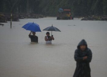 DUA pemuda mengharung banjir melebihi paras pinggang di Kampung Teladas di Kemaman, hari ini. - PUQTRA HAIRRY ROSLI