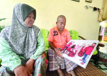 SAADAN Ismail bersama isterinya menatap gambar anak-anak dan sudah tidak sabar menunggu kepulangan mereka sempena Aidilfitri minggu depan di Kampung Jawi 100, Sungai Padang, Arau, Perlis. - UTUSAN/NAZLINA NADZARI