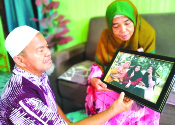 MOHD. Nadzir Mohamed bersama isteri, Zainun Sulaiman menetap gambar tiga anak perempuan mereka untuk melepaskan rindu selepas tiga beradik terbabit maut terkena renjatan elektrik dalam kejadian pada 19 Disember lalu di Kampung Bendang Surau, Tumpat, Kelantan. – UTUSAN/ROHANA ISMAIL