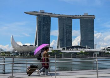 PENDUDUK sedang berjalan di sebuah jambatan berlatar belakang Marina Bay di Singapura. - AFP