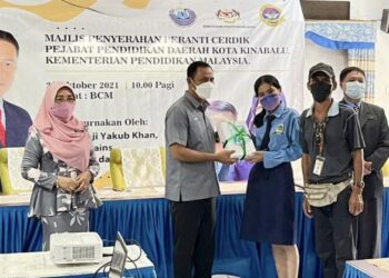 YAKUB KHAN (dua kiri) menyampaikan peranti kepada salah seorang pelajar SMK Kolombong di Kota Kinabalu hari ini.