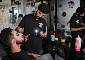 TUKANG gunting rambut terpaksa menggunakan lampu dari telefon bimbitnya selepas berlaku gangguan bekalan elektrik di Hamra, Beirut. – AFP