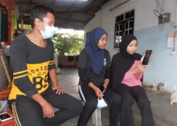 AMIRUL Hilmi Mohd. Shukri bersama Nur Amira Natasya (kanan) dan Nur Amanina Hazwani melihat gambar arwah ibu dan bapa mereka di dalam telefon bimbit ketika ditemui di Kampung kuala Ruat, Yan, Kedah, semalam. – UTUSAN/OTHMAN YAHAYA