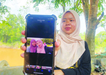 NUR Wahida Zailan menunjukkan gambarnya bersama Nur Hafizah. Adiknya itu  masih belum ditemukan selepas hilang dihanyutkan arus deras ketika melalui jambatan gantung Kampung Aur, Bukit Ibam di Muadzam Shah, Pahang. – UTUSAN/ DIANA SURYA ABD WAHAB