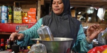 SEORANG penjual menimbang satu beg minyak masak di pasar tradisional di Jakarta.-AFP