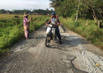 SEORANG penduduk meratakan batu yang disumbangkan oleh orang ramai untuk menutup permukaan jalan rosak di Kampung But, Ketereh, Kota Bharu, Kelantan. UTUSAN/ROSMIZAN RESDI