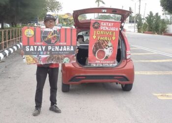 MUHAMMAD Hanif Nordin memegang sepanduk ketika menjual sate di tepi jalan Klebang Besar Melaka. - UTUSAN/AMRAN MULUP