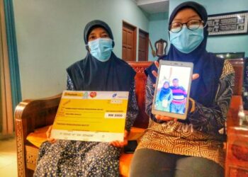 NUR Adriana Aleeya Zulkifli (kanan) memegang gambar ibu bapa yang meninggal dunia akibat wabak Covid-19 di sisi neneknya, Jormiah Nusi, 65, di Semanggol dekat Bagan Serai, Perak, hari ini. - FOTO/WAT KAMAL ABAS
