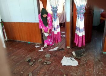 AMINAH Abdullah mengutip bahagian siling dan bumbung rumahnya yang pecah selepas dibadai ribut di Kampung Padang Embun, Pasir Mas, Kelantan kelmarin.-UTUSAN/ROHANA MOHD. NAWI