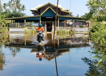 SEORANG penduduk menunggang motosikal meredah air banjir termenung di halaman rumahnya di Bagan Datuk, Perak, semalam. - UTUSAN/AIN SAFRE BIDIN