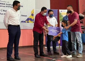 JAPLIN Akim (dua kiri) menyampaikan cek replika akaun simpanan SSPN kepada salah seorang murid, sambil disaksikan oleh Wan Saiful Wan Jan (dua kanan) di Kota Belud hari ini.