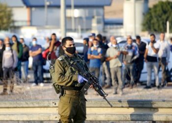 A member of the Israeli security forces stands guard as Palestinian workers are gathered to be turned back after they tried crossing illegally to Israel, at the checkpoint of Mitar, just south of the Palestinian village of al-Dahria, close to the West Bank city of Hebron, on October 11, 2020, amid a nationwide lockdown inforced by the Israeli authorities in a bid to stem a surge in coronavirus cases. (Photo by HAZEM BADER / AFP)