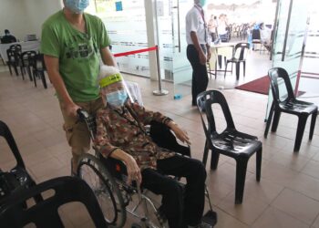 SEORANG warga emas ditemani anaknya menunggu untuk menerima vaksin Covid-19 di Pusat Pemberian Vaksin (PPV) Wakaf Bharu, Tumpat, Kelantan semalam. - UTUSAN/ZULHANIFA SIDEK