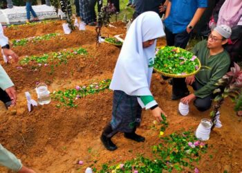 SITI Nur Khadijah Nasaruddin menabur bunga di pusara ibu dan empat adik beradiknya di Tanah Perkuburan Islam Kampung Paya Panjang di Padang Rengas hari ini. - UTUSAN