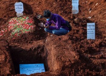 SEORANG lelaki berdoa di hadapan kubur ahli keluarganya yang meninggal dunia akibat Covid-19 di Pondok Rangon, Jakarta. - KOMPAS.COM