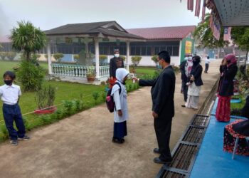 SEORANG guru  memeriksa suhu badan murid sebelum masuk ke kelas untuk memulakan sesi persekolahan awal tahun ini di Sekolah Kebangsaan Ulu Tembeling di Kampung Bantal di Jerantut semalam. 
– UTUSAN/HARIS FADILAH AHMAD