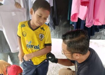 FARID Suwardi membantu salah seorang murid mengenakan pakaian sekolah terpakai yang dikumpulkan bagi membantu meringankan beban ibu bapa di Nibong Tebal, Pulau Pinang baru-baru ini. - UTUSAN/SITI NUR MAS ERAH AMRAN