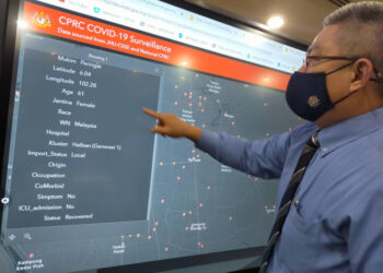 PDr. Adham Baba menunjukkan monitor pengawasan dan pemantauan CPRC Covid-19 kepada wartawan Utusan Malaysia, Maisarah Sheikh Rahim ketika  ditemu bual di Kementerian Kesihatan, Putrajaya 
baru-baru ini. – UTUSAN/FAISOL MUSTAFA