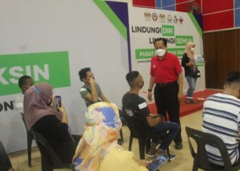 AHMAD Maslan (berdiri) berbual bersama penerima vaksin di PPV Dewan Serbaguna Benut di Pontian, Johor. - FOTO/MUHAMMAD ZIKRI