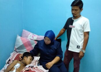 MOHD. FADLY Zakaria (kanan) dan Rosniza Hussin (tengah) melihat keadaan Muhammad Farhan Mohd. Fadly yang terlantar sakit di kediaman mereka di Peringgit, Melaka akibat kegagalan buah pinggang sejak 10 tahun lalu. - UTUSAN/MUHAMMAD SHAHIZAM TAZALI