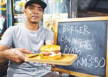 FADLI Mohd. Nor mengakui tertekan dengan kenaikan harga bahan mentah sekali gus mendorongnya menetapkan harga baharu burger di gerainya di Kampung Chabang Empat, Tumpat, Kelantan. 
– UTUSAN/ROHANA ISMAIL