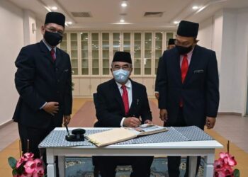 AWANG Hashim (kanan) menyaksikan Mohd. Ali Mohd. Rustam menurunkan tandatangan pada buku pelawat ILP Selandar, Alor Gajah, Melaka.