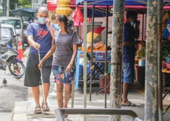 Warga OKU yang buta dibantu orang awam apabila laluan panduan trek pejalan kaki dihalang oleh  peniaga yang mendirikan gerai  di Jalan Sultan Abdul Samad, Brickfields, semalam. – UTUSAN/AMIR KHALID