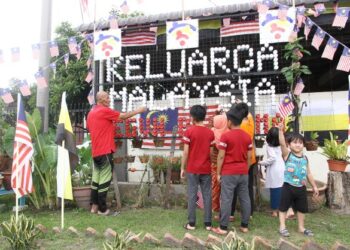 JAMALUDDIN Ahmad ditemani cucu-cucunya memasang Jalur Gemilang di hadapan rumah sempena sambutan Hari Kebangsaan di Kampung Tersusun Tasek di Ipoh, Perak semalam. – UTUSAN/MUHAMAD NAZREEN SYAH MUSTHAFA
