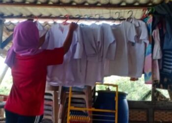 HABIBAH Yahya menyidai baju sekolah anak-anaknya yang dibasuh semula akibat terkena lumpur banjir di rumahnya di Kampung Seberang Batu Badak, Segamat.
