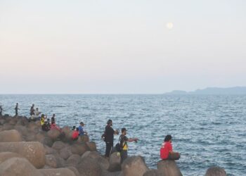 SEBAHAGIAN pemancing berkumpul di kawasan benteng pemecah ombak di Pantai Rhu Renggeh, Chendering, Kuala Terengganu bermula pukul 7 malam untuk mencandat sotong jarum. - UTUSAN/PUQTRA HAIRRY ROSLI
