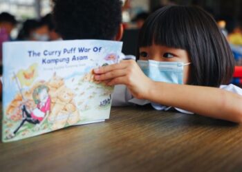 Seorang kanak-kanak khusyuk membaca 'The Curry Puff War Of Kampung Asam'. Buku mengisahkan manfaat bekerjasama.