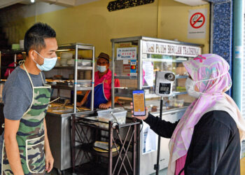 PEKERJA restoran, Mamat Abdul Wahab (kiri) memeriksa sijil digital MySejahtera pelanggannya sebelum membenarkan memasuki premis di Kuala Terengganu, semalam. – UTUSAN/PUQTRA HAIRRY