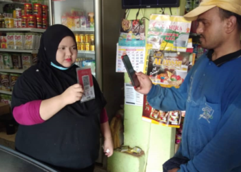 Seorang pekerja ladang FGV mengimbas kod QR pembayaran e-wallet ketika membeli barang di sebuah kedai runcit.