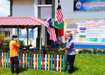 ABD. Manaf Mat (kanan) dibantu kakitangan pembersihan sekolah sedang memasang Jalur Gemilang di tepi padang Sekolah Kebangsaan Hulu Tembeling di Jerantut, Pahang. - FOTO/HARIS FADILAH AHMAD