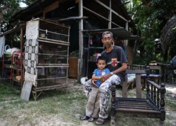 HAZIMI Ayob bersama salah seorang anaknya, Muhammad Rayan Firdaus Abdullah di hadapan bangsal usang dan serba kekurangan yang dijadikan rumah mereka di Kampung Kubur Panjang, Pendang di sini.- UTUSAN/ SHAHIR NOORDIN