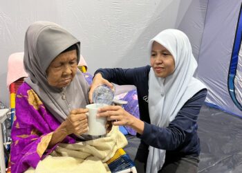 NORISAN ALI membantu menyiapkan keperluan ibunya ketika ditempatkan di PPS di IKTBN Pagoh, Muar.