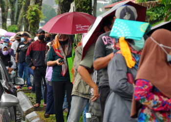 Orang ramai beratur dan menjaga SOP walau dalam keadaan hujan untuk mendapatkan pek keperluan asas sempena Program Bank Makanan di Dewanraya Taman Perbadanan Islam, Kebun Teh disini. -UTUSAN/RAJA JAAFAR ALI
