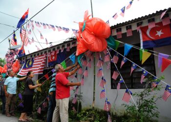 AZMI Basiran (kanan) bersama penduduk kampung bekerjsama memasang bendera dan replika bunga raya di Kampung Sepakat Baru, Johor Bahru semalam. - UTUSAN/RAJA JAAFAR ALI 
pemberita : faizal
