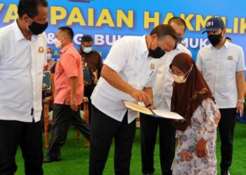 HASNI Mohammad menerangkan sesuatu kepada salah seorang penerima hak milik tanah bagi Kampung Bukit Nyamuk dan Kampung Seri Maju Jaya di Renggam, Kluang, Johor. -UTUSAN/RAJA JAAFAR ALI