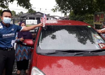 RAZRUL Anwar Rusli (kiri) memasang Jalur Gemilang pada sebuah kereta ketika program Semarak Merdeka Kibaran Jalur Gemilang di Larkin, Johor Bahru, semalam.