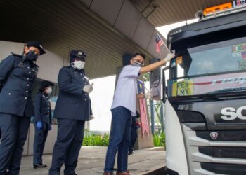 MD Derick Basir melekatkan Jalur Gemilang pada sebuah lori mengangkut kargo di Johor Port.